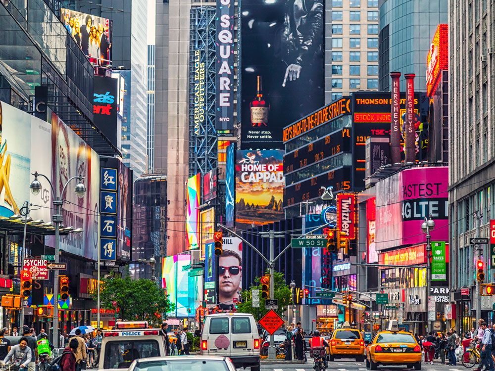 Busy Times Square scene filled with tourists, cars, and advertisements on buildings