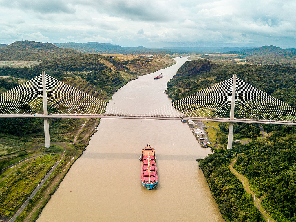 Aerial view of bridge spanning over Panama Canal and cargo ship passing underneath