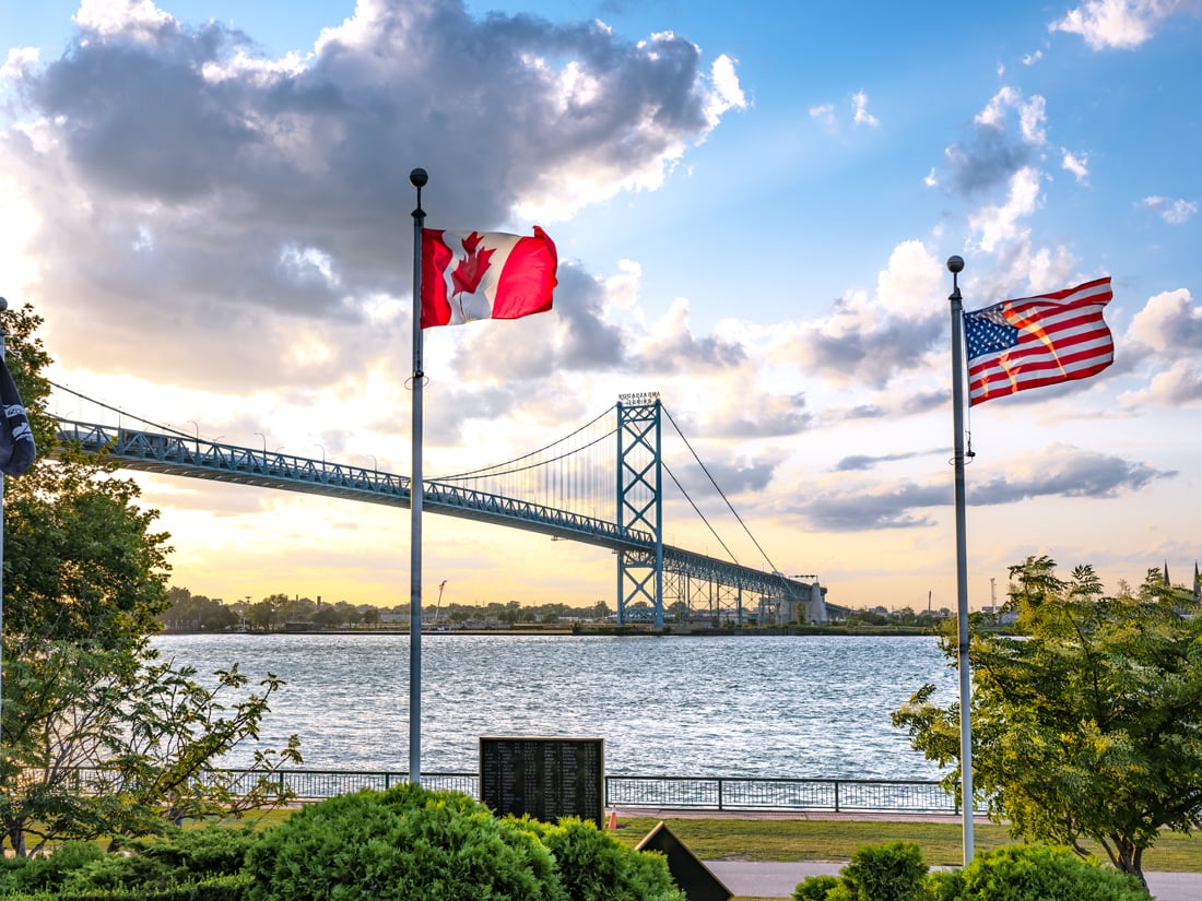 Flags of Canada and the United States along the Detroit River with the Ambassador Bridge in the background