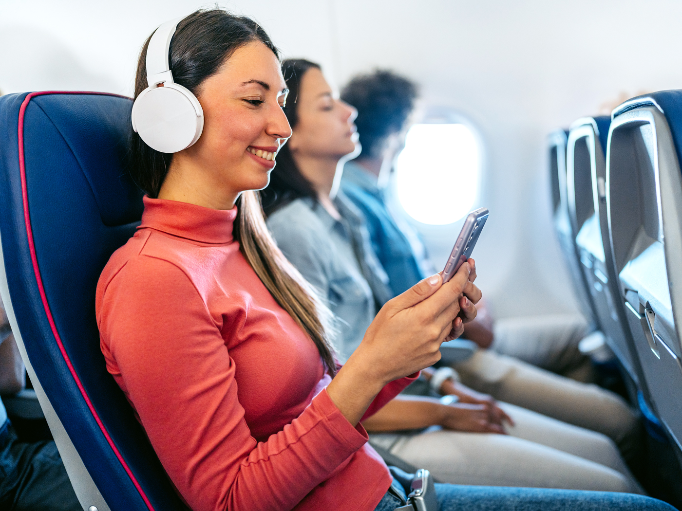 Airplane passenger wearing noise-canceling headphones and looking at cellphone