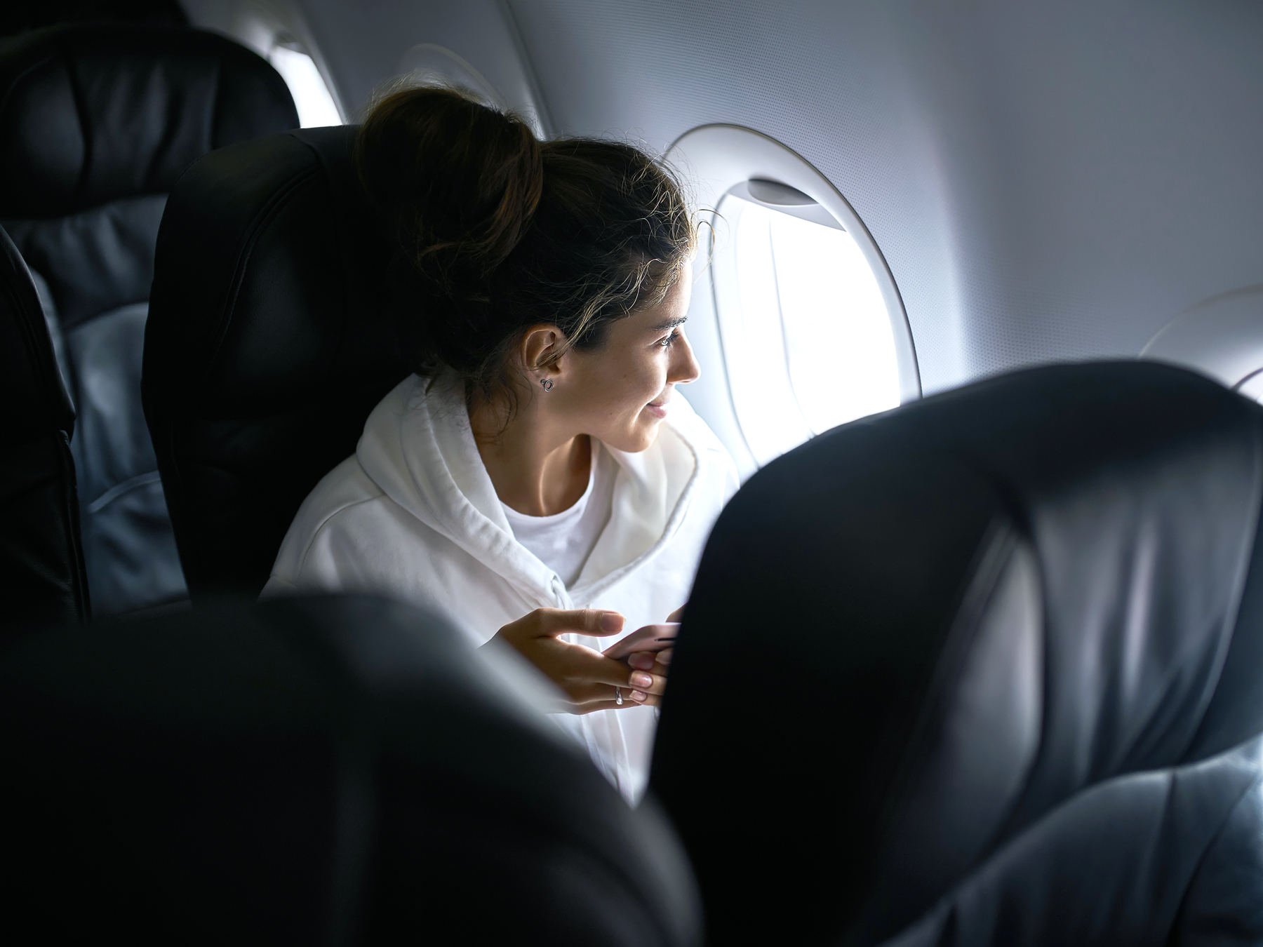 Airplane passenger in hoodie looking out window