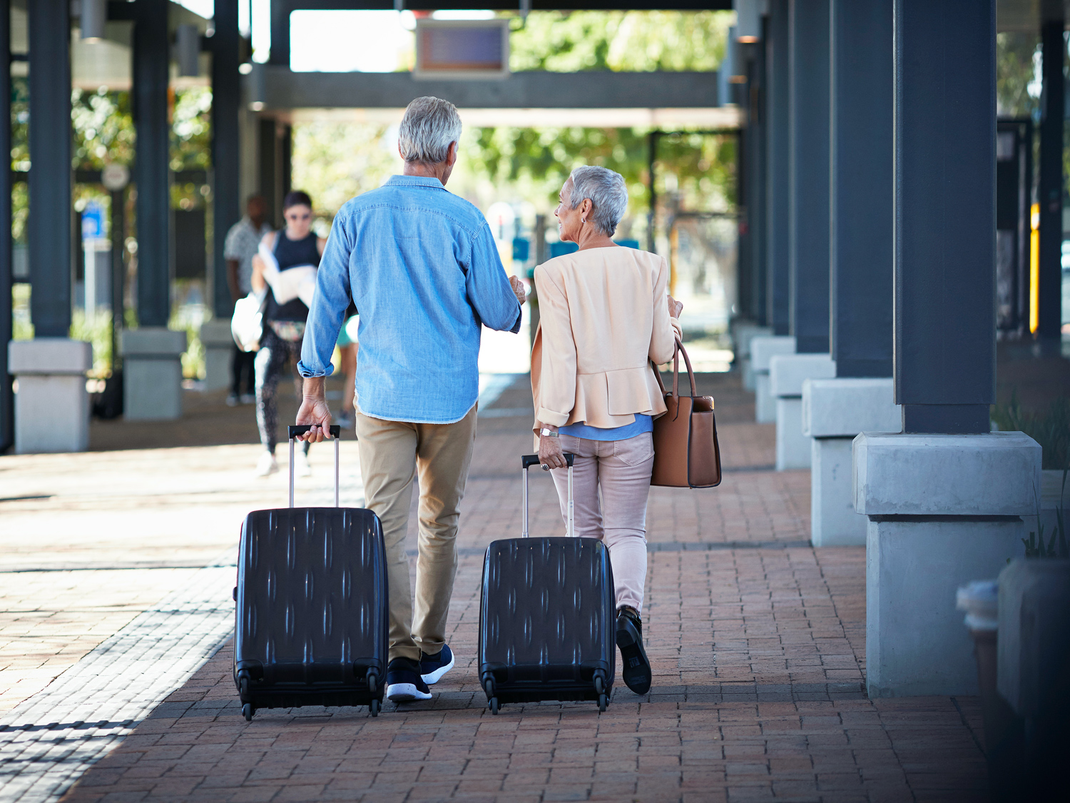 Man and woman rolling suitcases on sidewalk