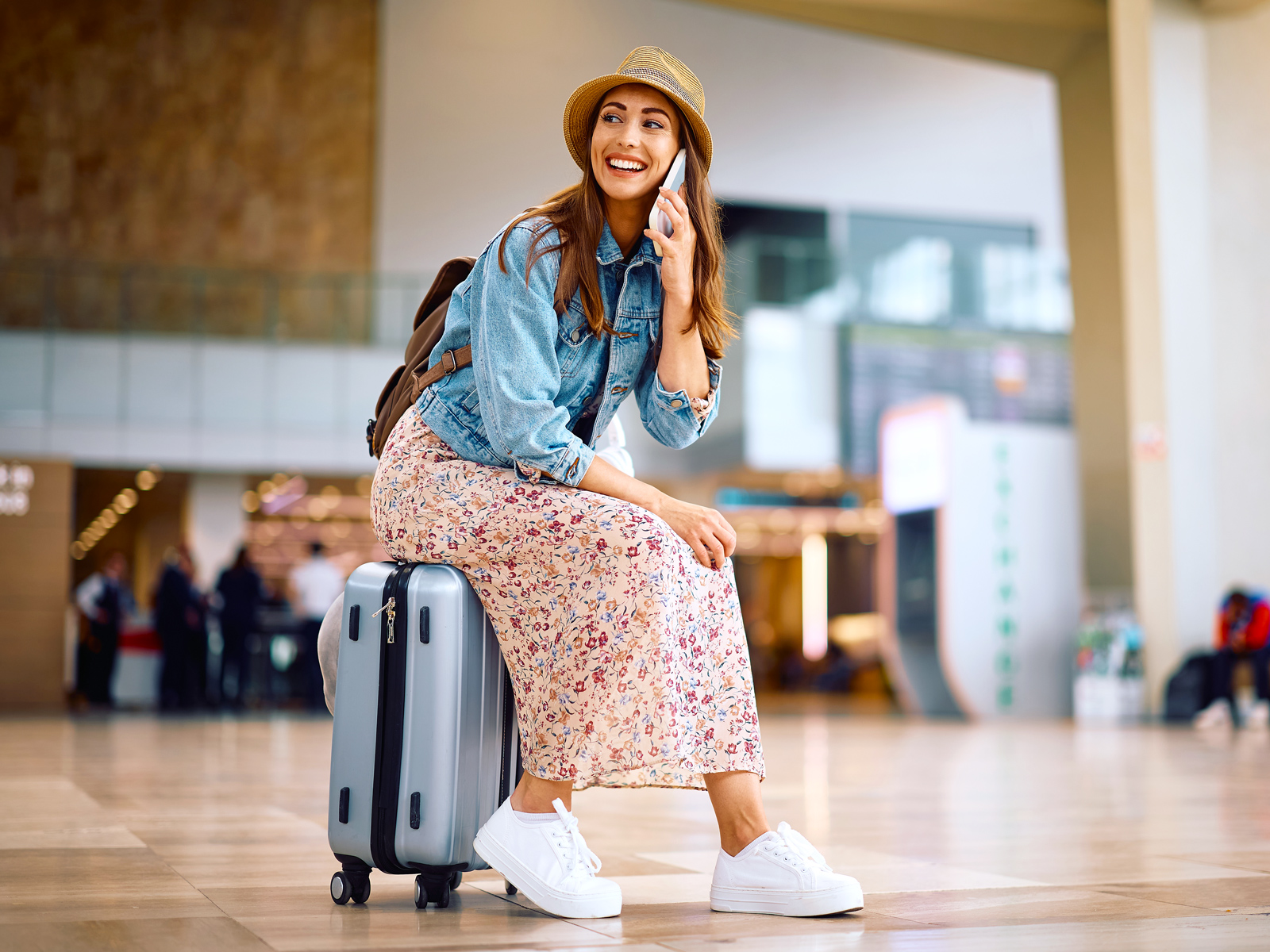 Woman talking on phone and sitting on suitcase in airport