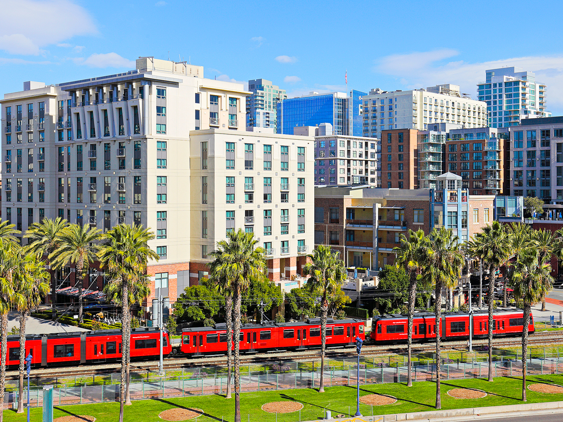 Red tram passing by palm trees and high-rise buildings in San Diego, California