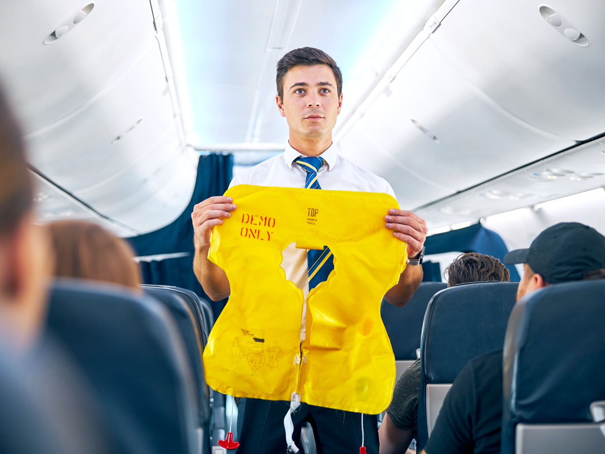Flight attendant performing safety demonstration in aircraft aisle