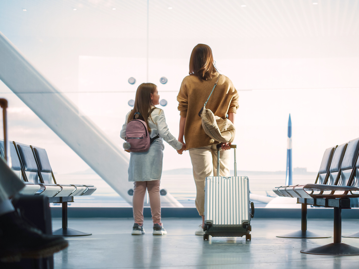 Mother and daughter holding hands looking out airport window
