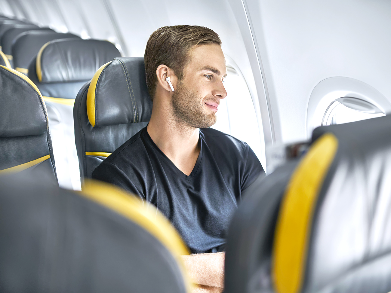 Airline passenger in seat wearing Bluetooth headphones
