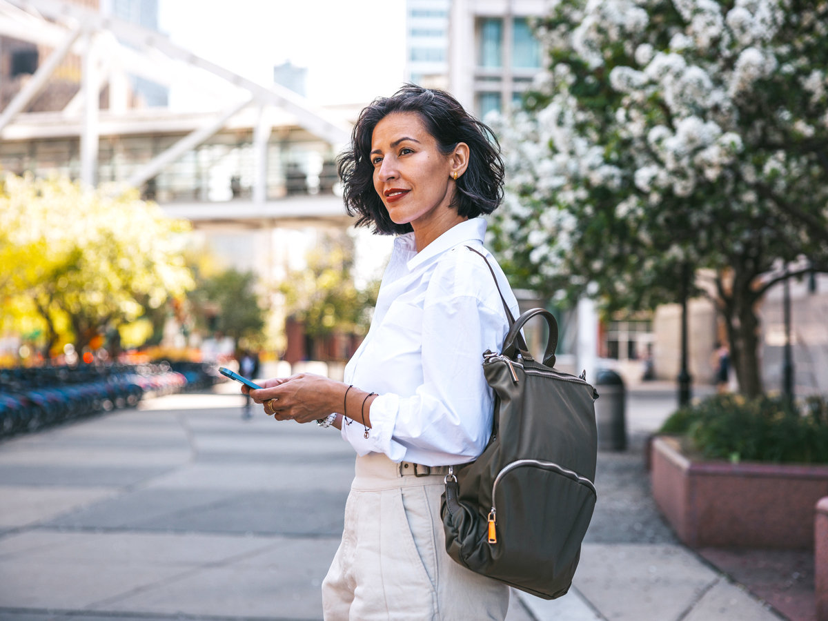 Woman standing on street with backpack and phone