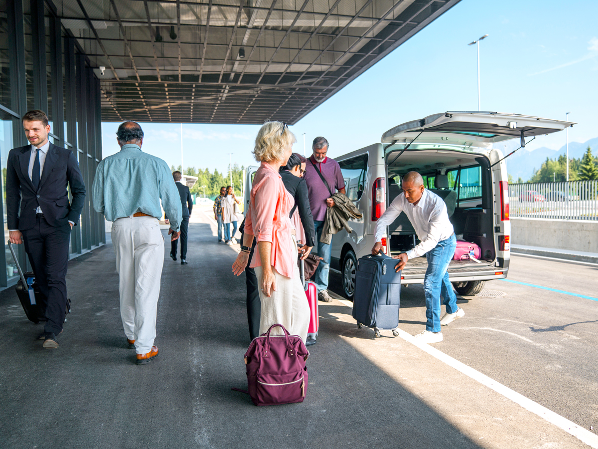 Travelers putting luggage into shuttle at airport curbside pick-up