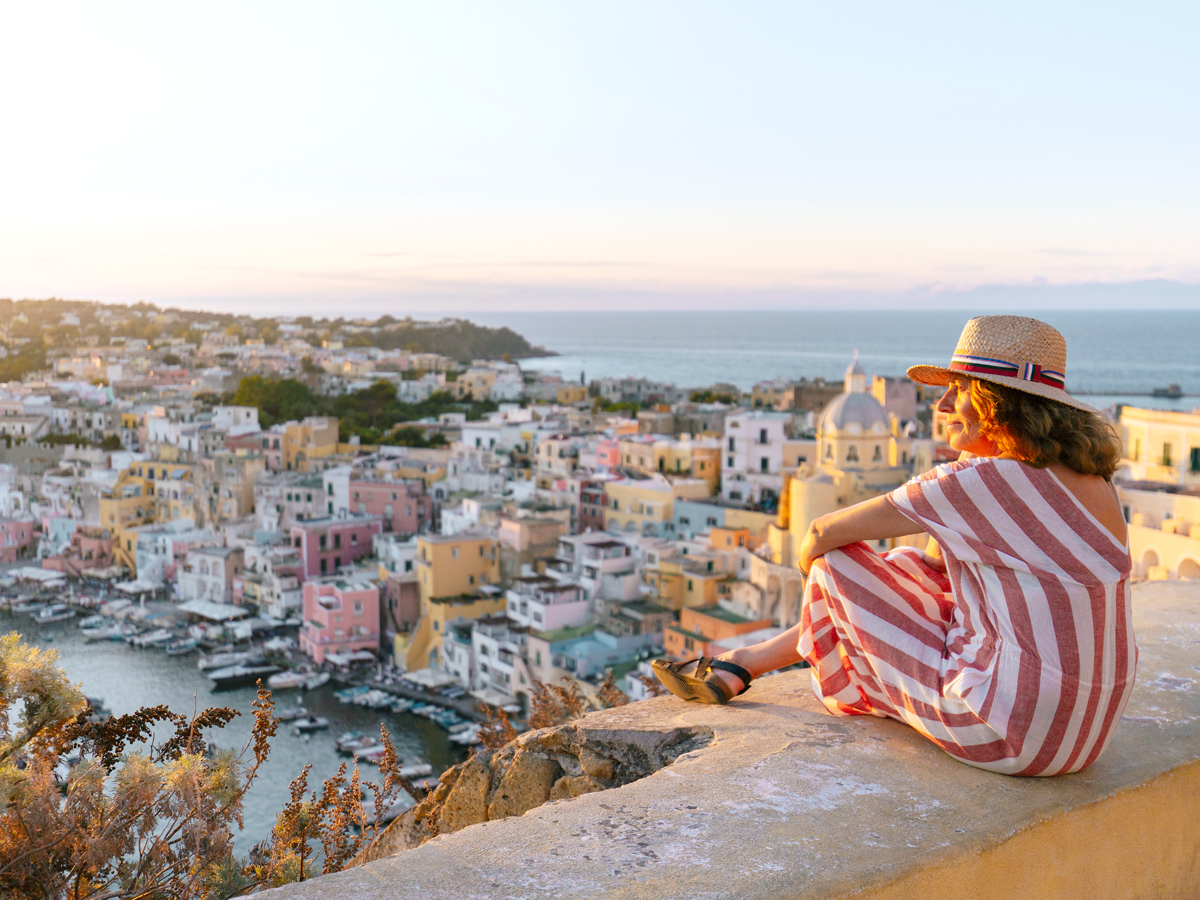 Woman sitting on wall overlooking island of Procida, Italy