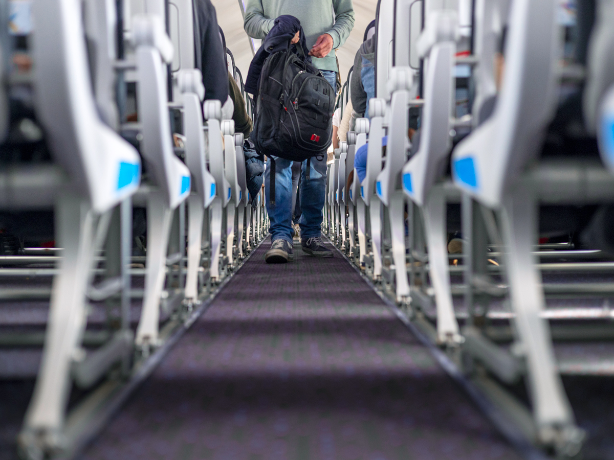 Airline passenger holding backpack walking through aircraft aisle