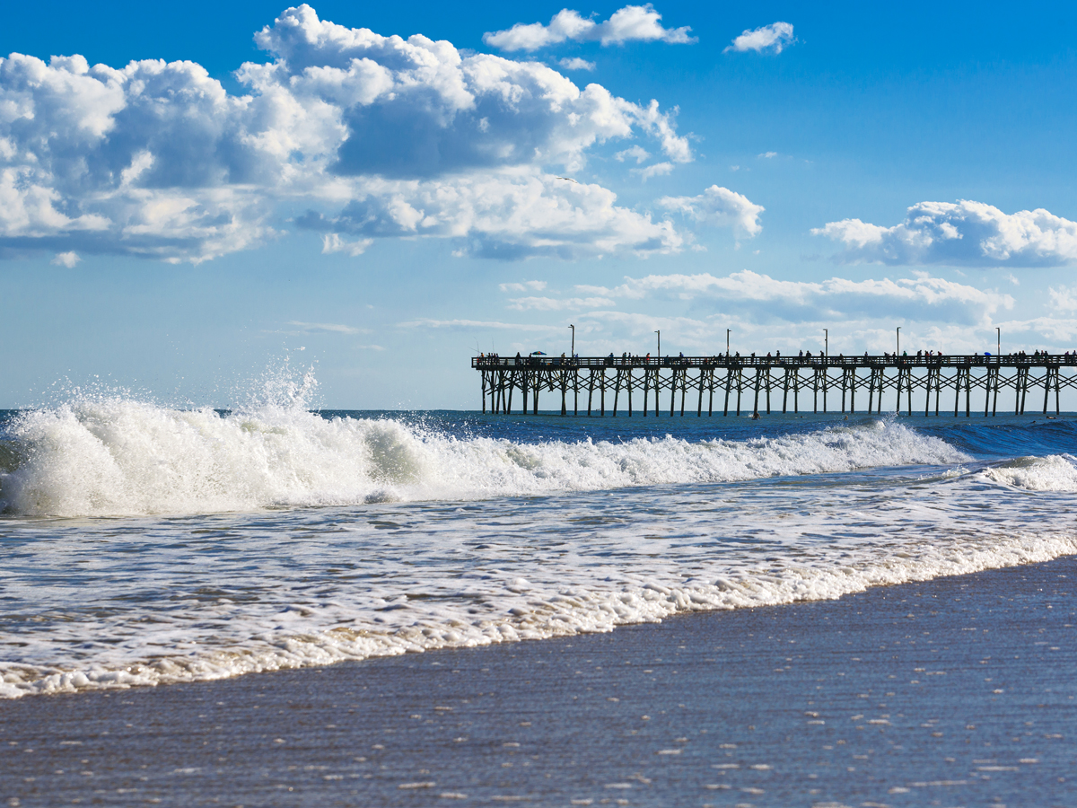 Pier extending into Atlantic Ocean with waves crashing on beach on Topsail Island, North Carolina