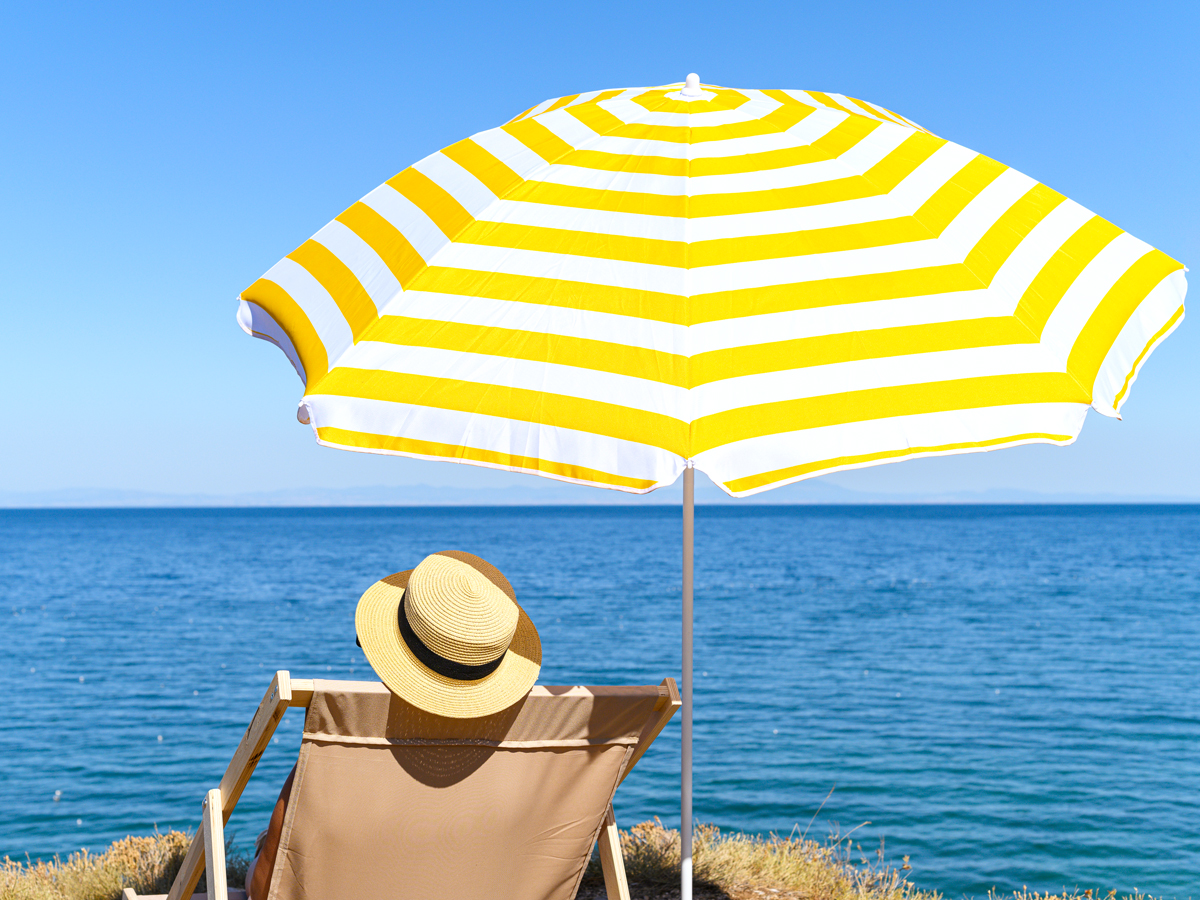 Person sitting under umbrella looking at the ocean