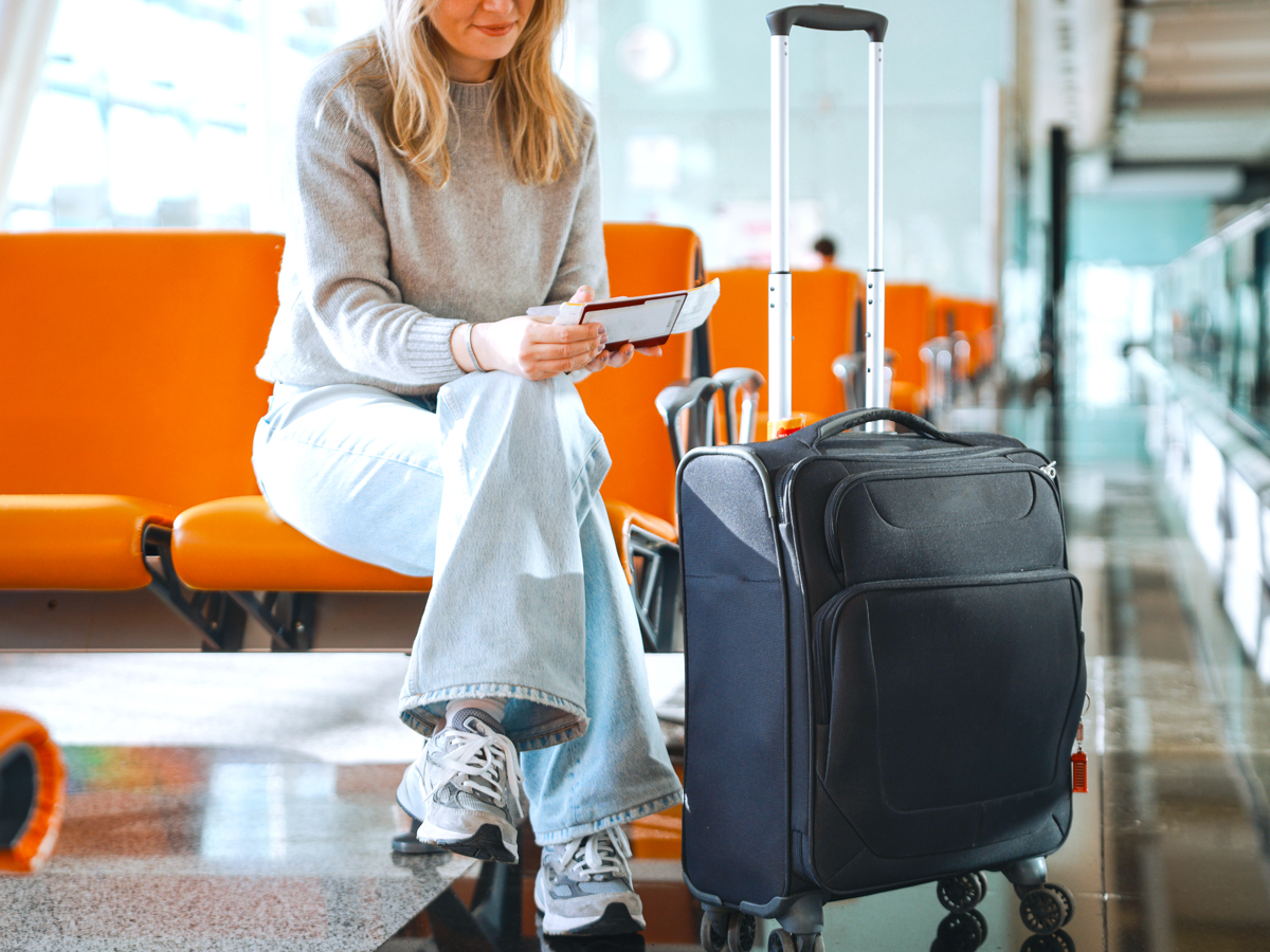 Passenger sitting at gate with suitcase and boarding pass