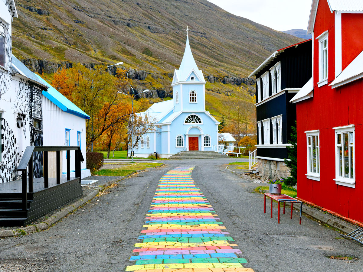 Rainbow pathway leading to blue church in Iceland