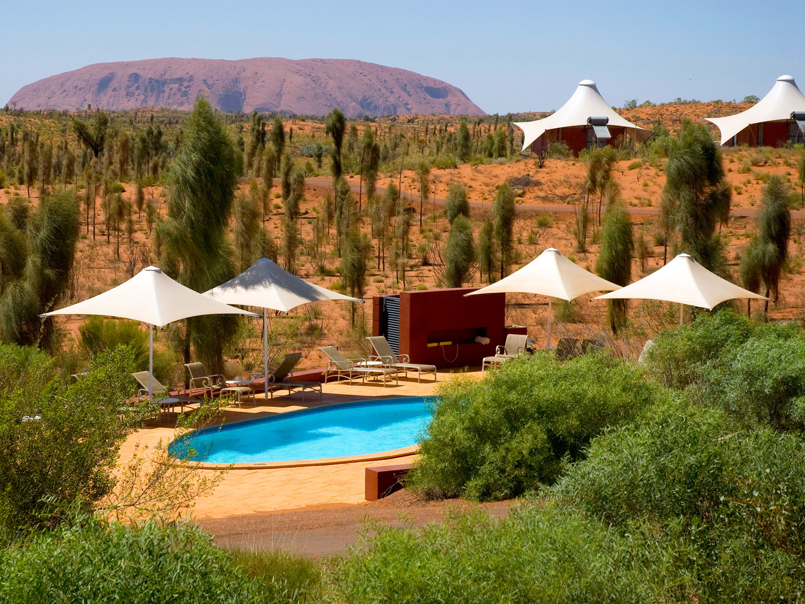Swimming pool and glamping tents with Uluru rock formation in background