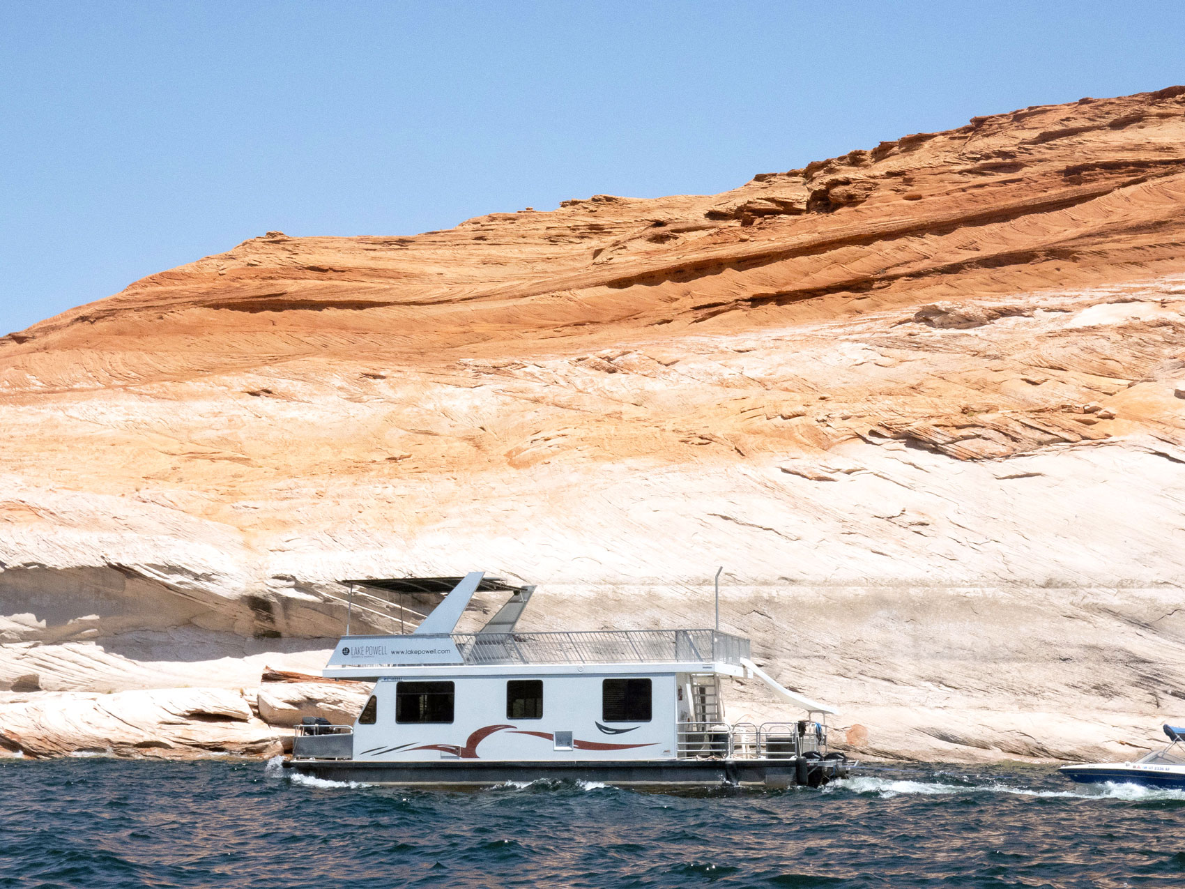 Houseboat cruising past sandstone cliffs along Lake Powell