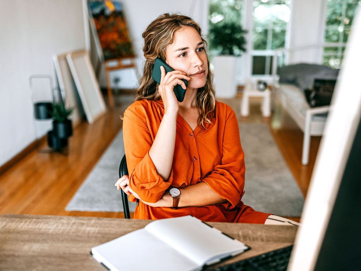 Woman sitting at desk with open notebook talking on phone