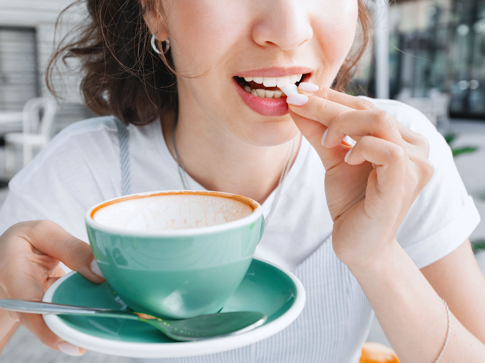Woman holding coffee cup and placing bubble gum in mouth