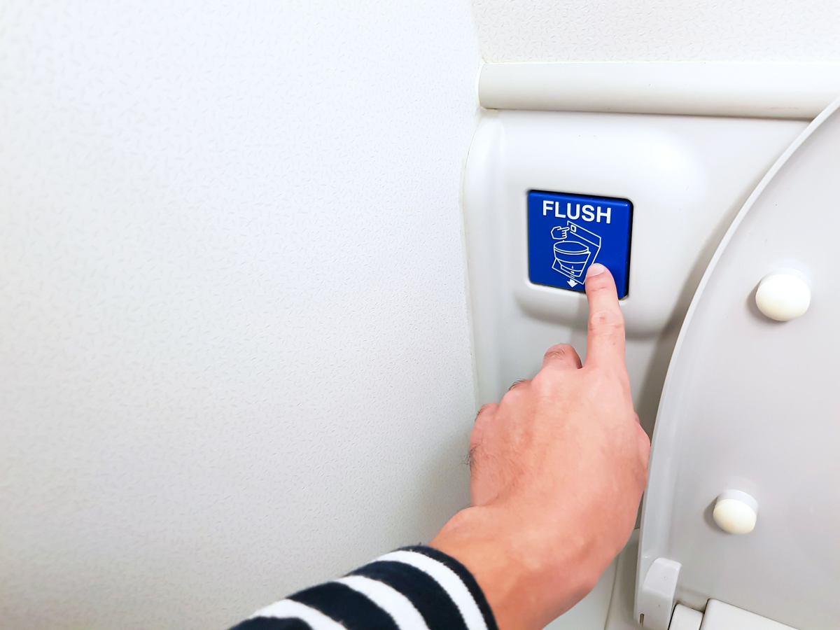 Passenger pressing "flush" button in airplane lavatory