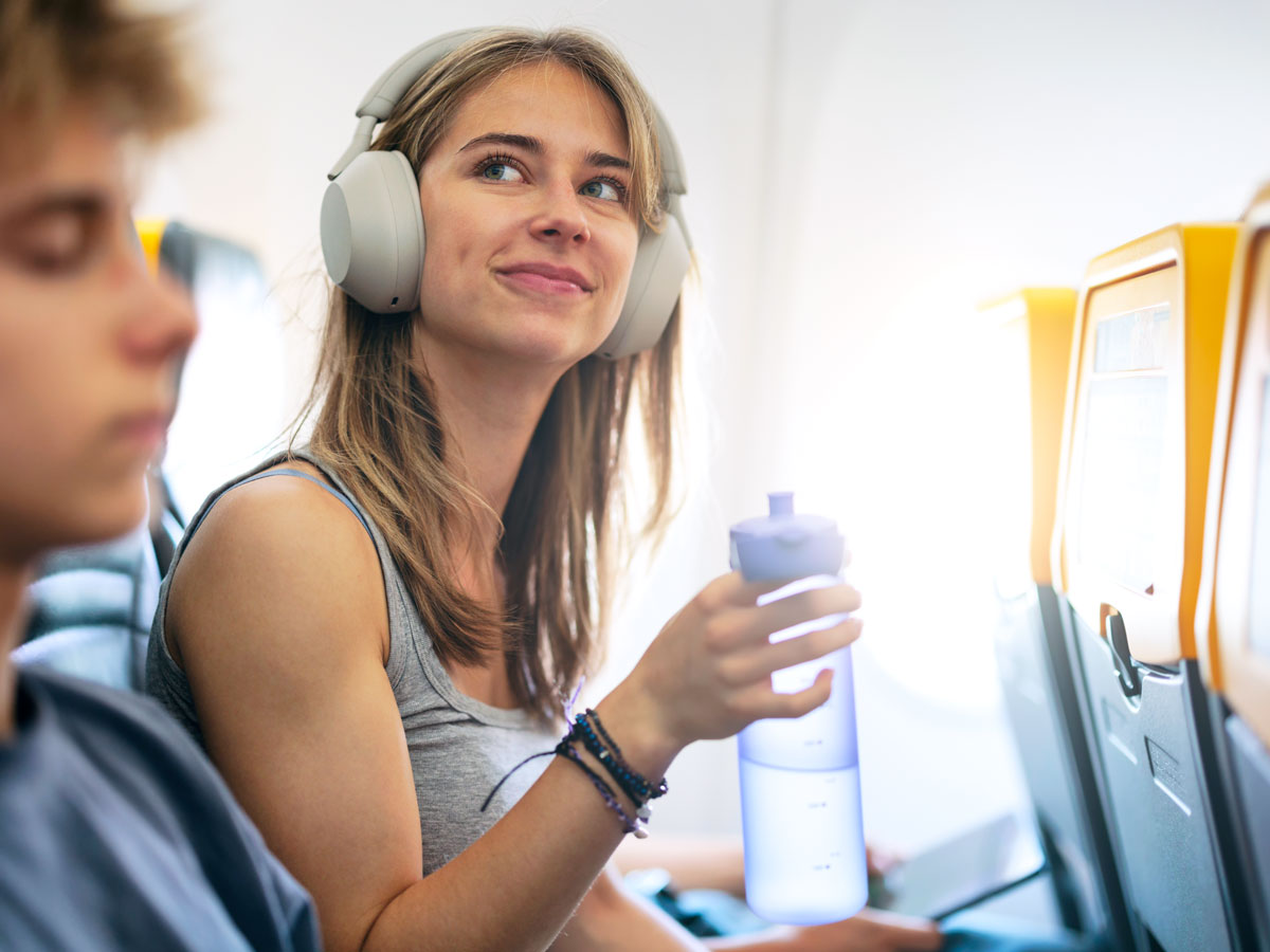Passenger in airplane seat wearing headphones and drinking from reusable water bottle