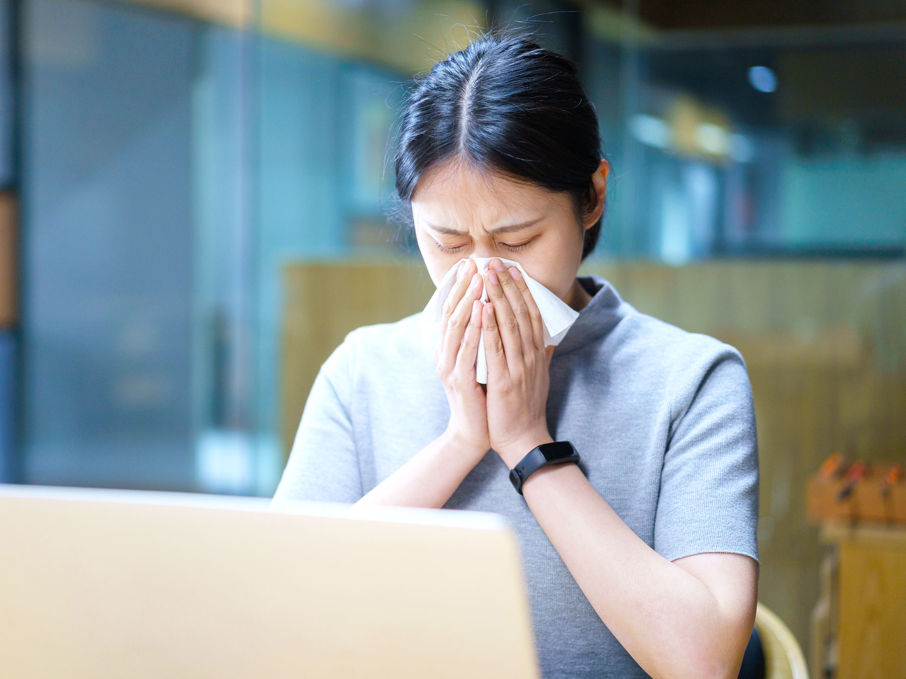 Woman sitting at computer and blowing nose