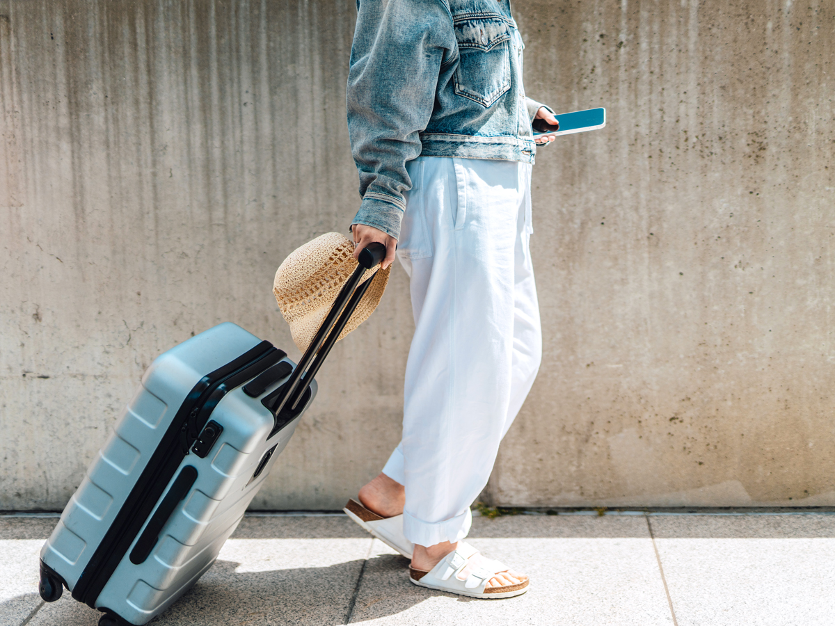 Traveler wearing sandals rolling suitcase down street