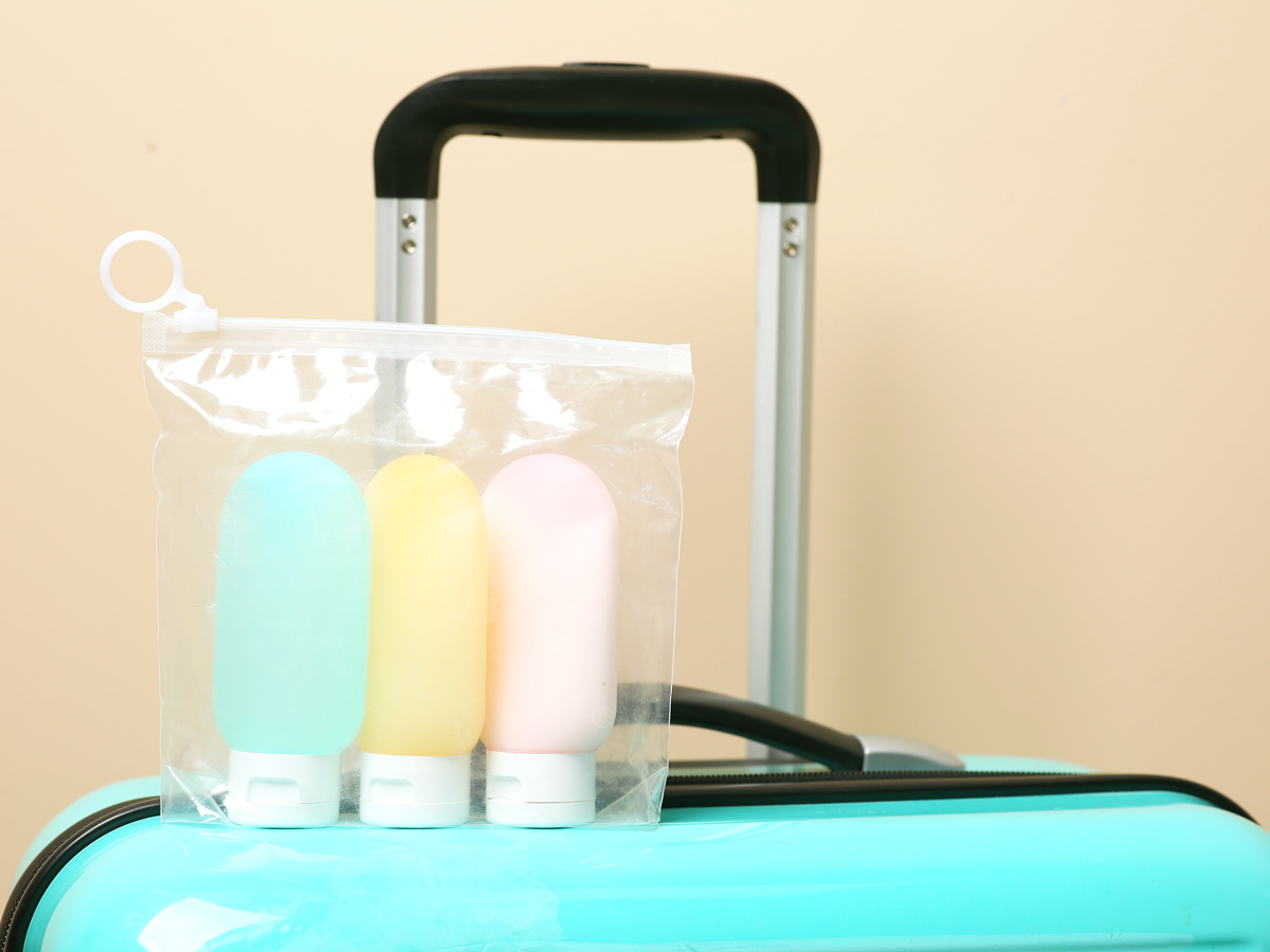 Reusable travel-sized toiletry containers inside clear plastic bag atop suitcase