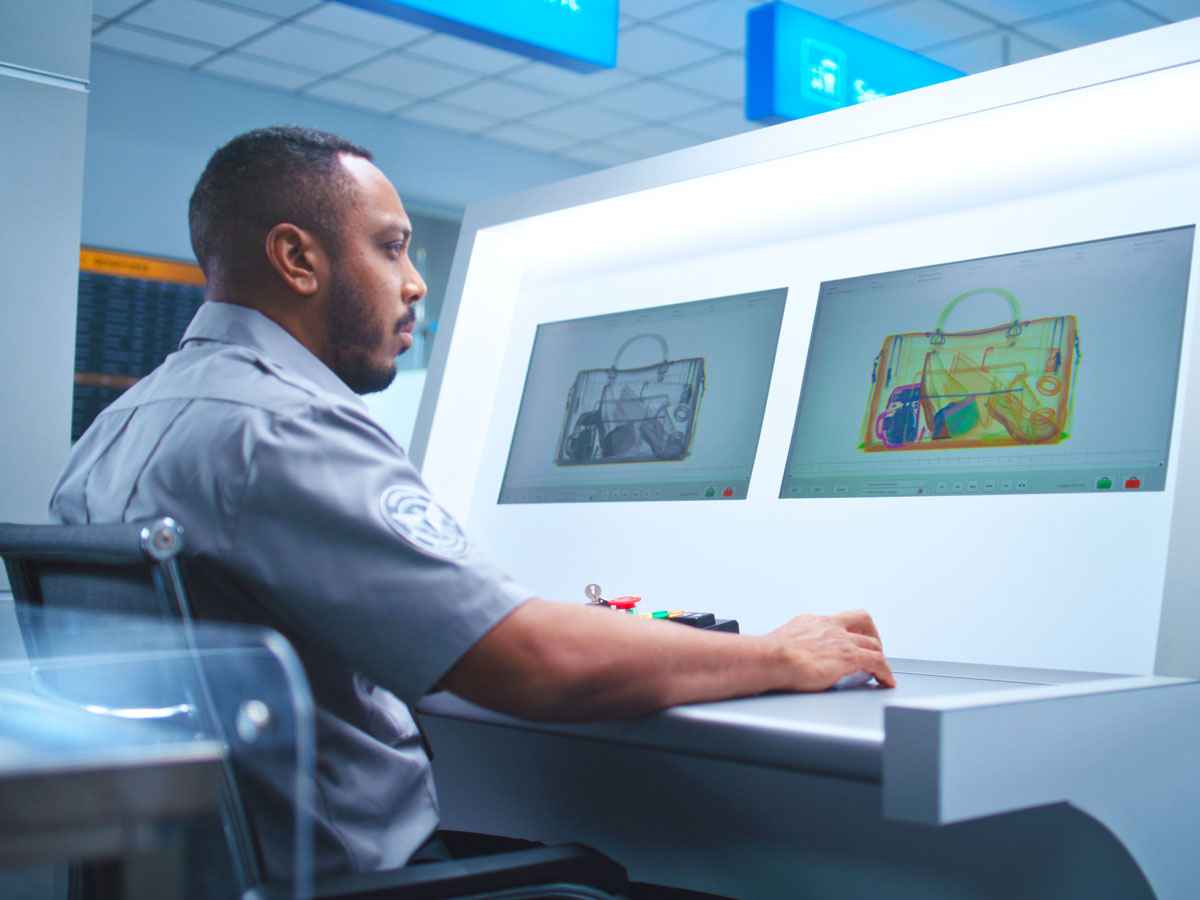 Security officer reading X-ray scan of baggage on conveyor belt