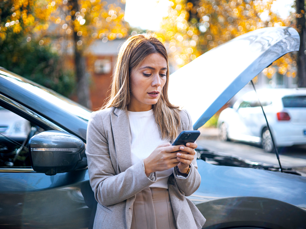 Woman using cellphone next to car with open hood