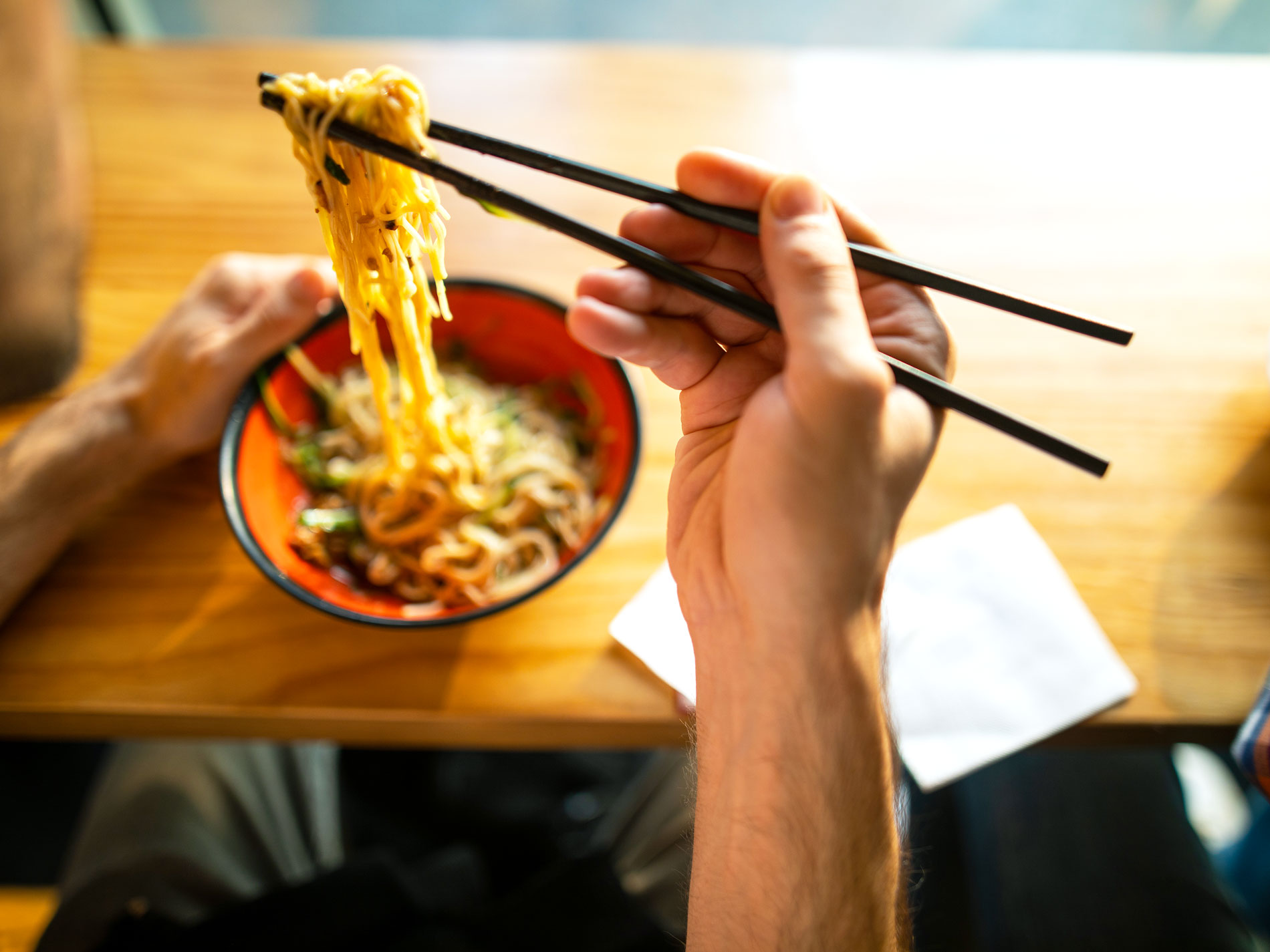 Person using chopsticks to eat bowl of noodles