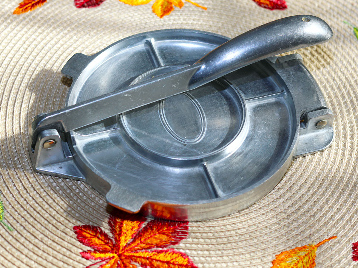 A metallic tortilla press on a placemat