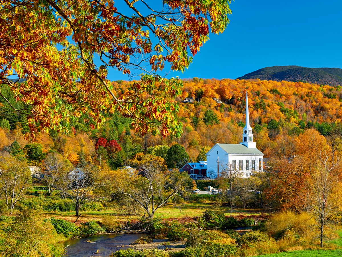 White church with tall steeple surrounded by fall foliage in Stowe, Vermont