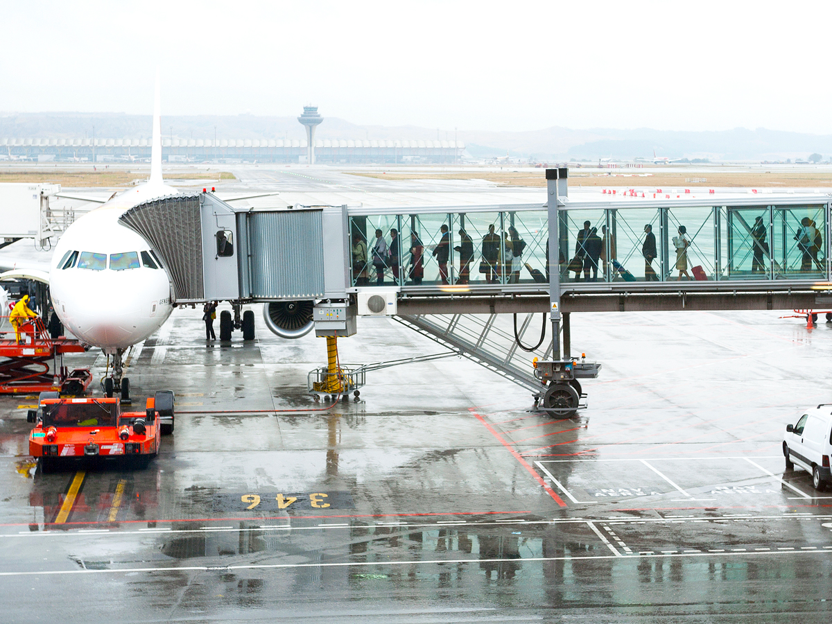 Passengers waiting in glass jet bridge to board aircraft on a rainy day