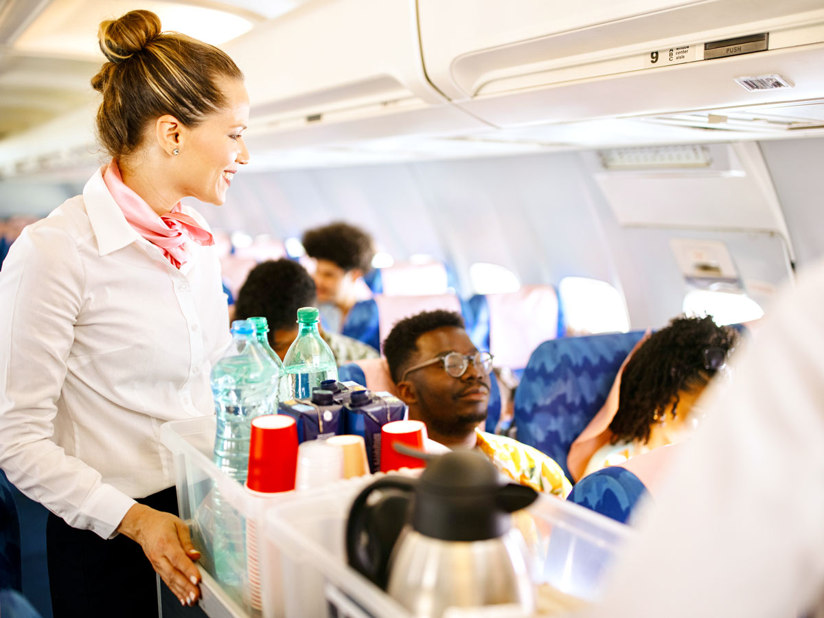 Flight attendant with cart in aisle serving passengers