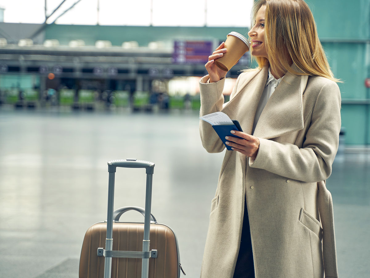 Woman standing in airport terminal with suitcase and a cup of coffee