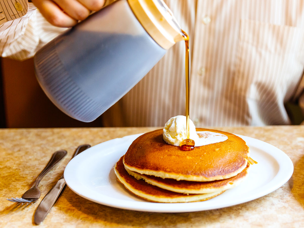 Person pouring maple syrup on stack of pancakes
