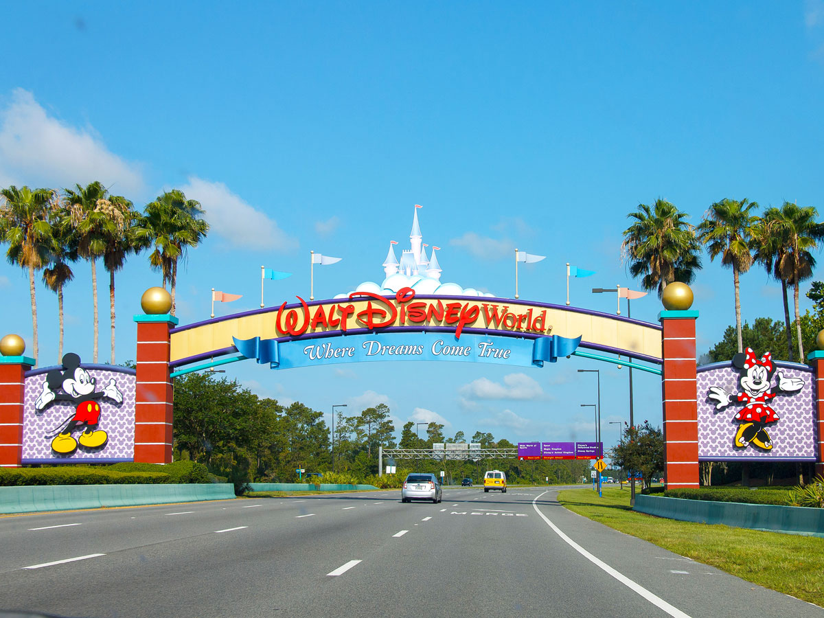 Sign over roadway for Walt Disney World with slogan "Where Dreams Come True"