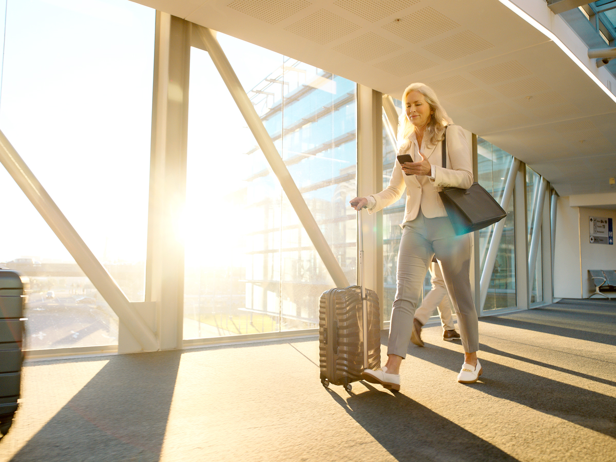 Passenger rolling suitcase through airport while looking at cellphone