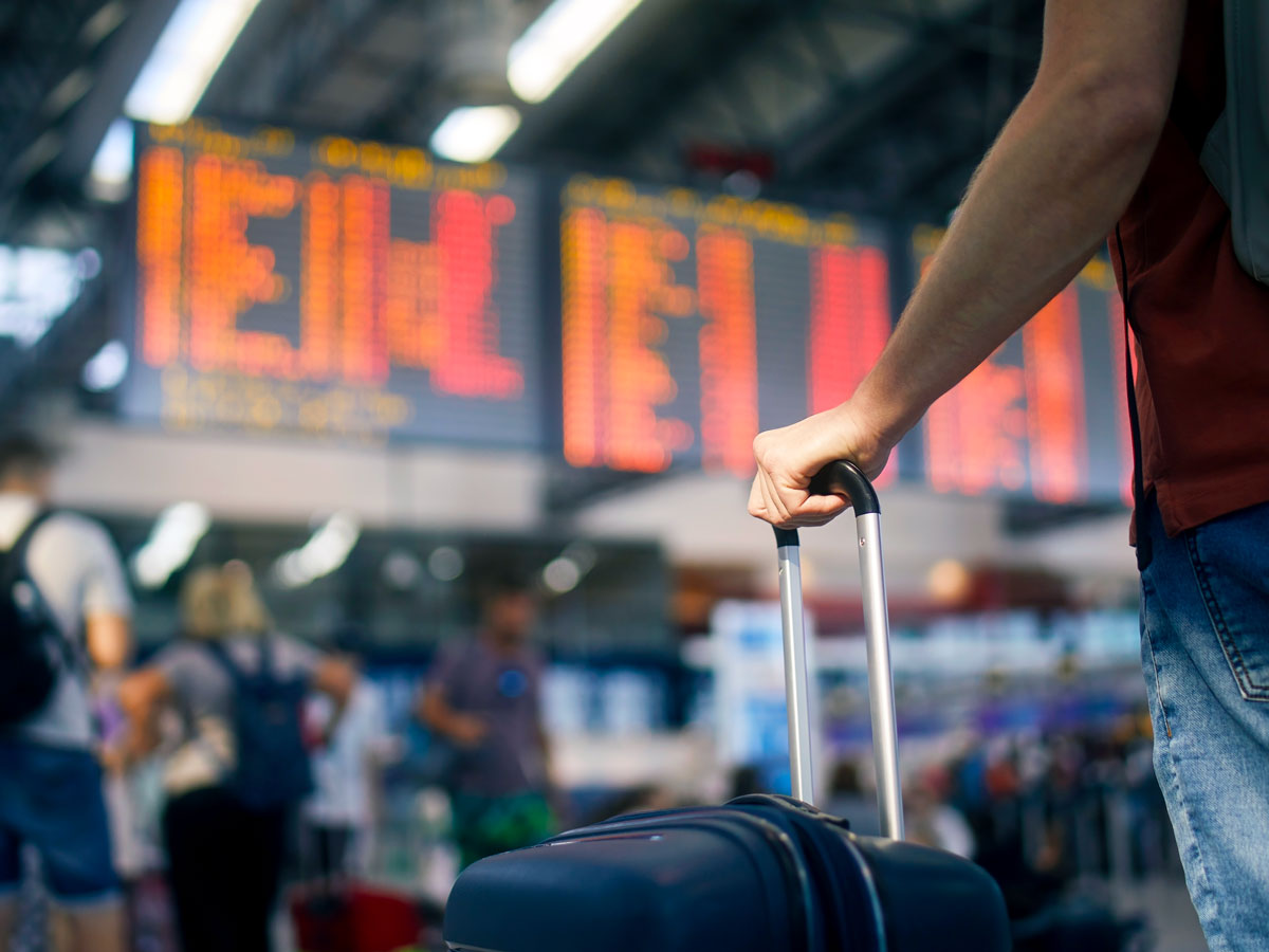 Traveler with hand on suitcase looking at departures board