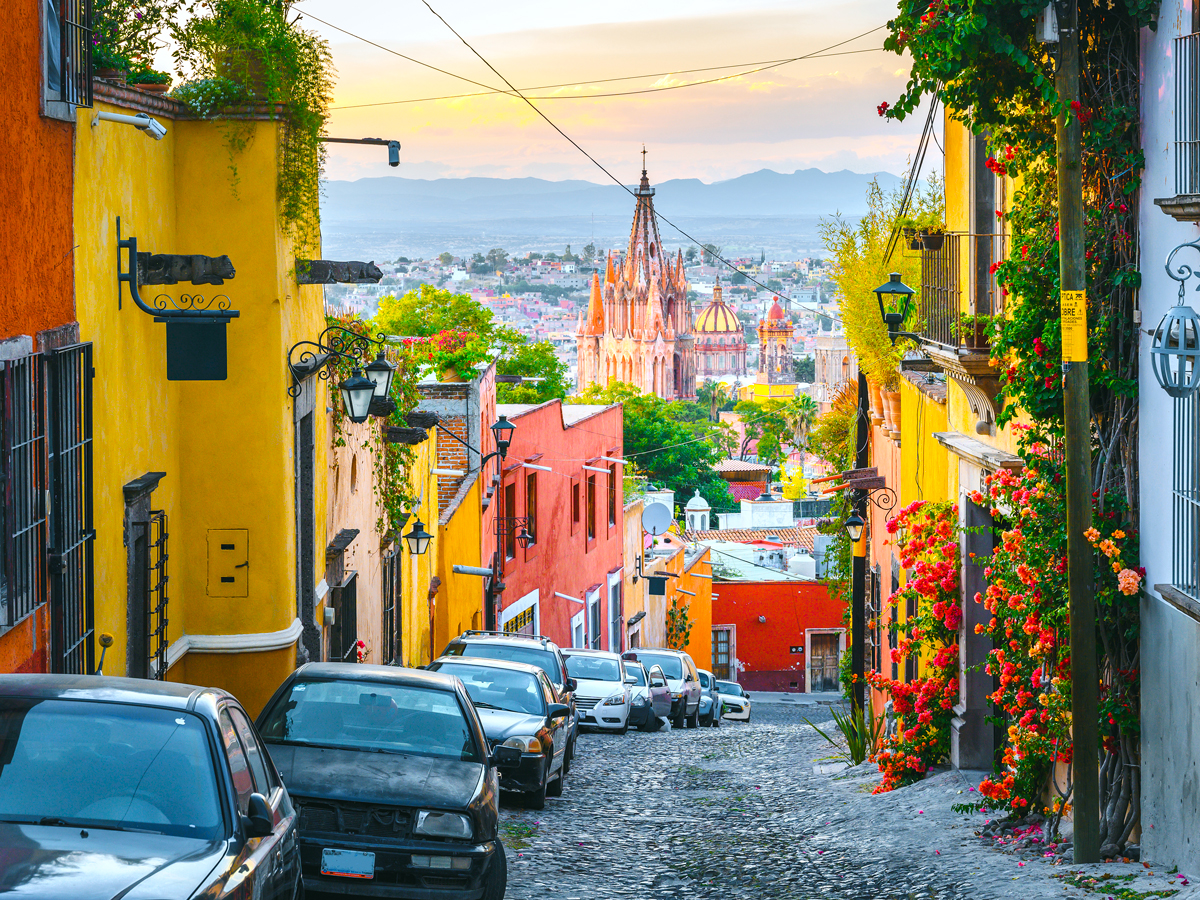 Cars parked beside brightly painted buildings on hilly street overlooking San Miguel de Allende, Mexico