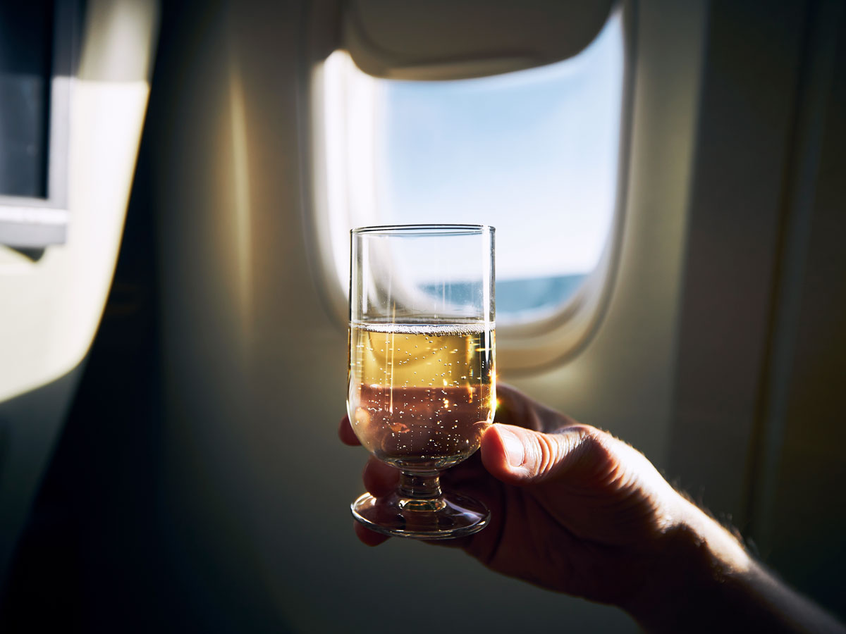 Passenger holding glass of sparkling wine in front of airplane window