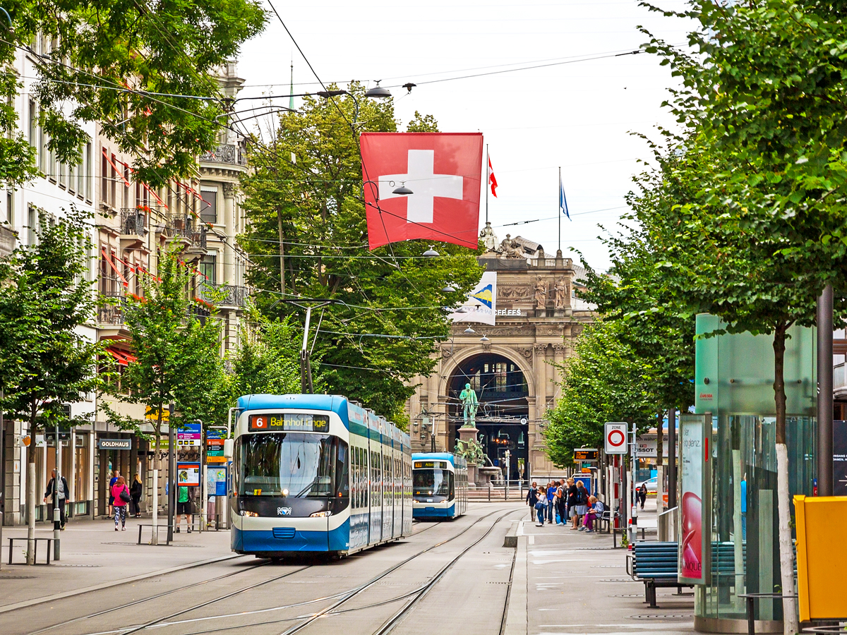 Trams on Zurich street with Swiss flag flying overhead