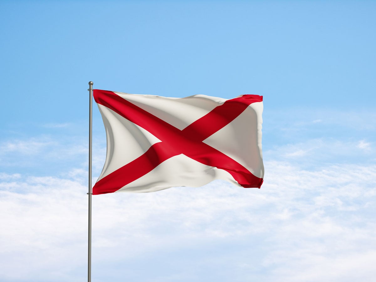Alabama flag flying with partly cloudy skies in background