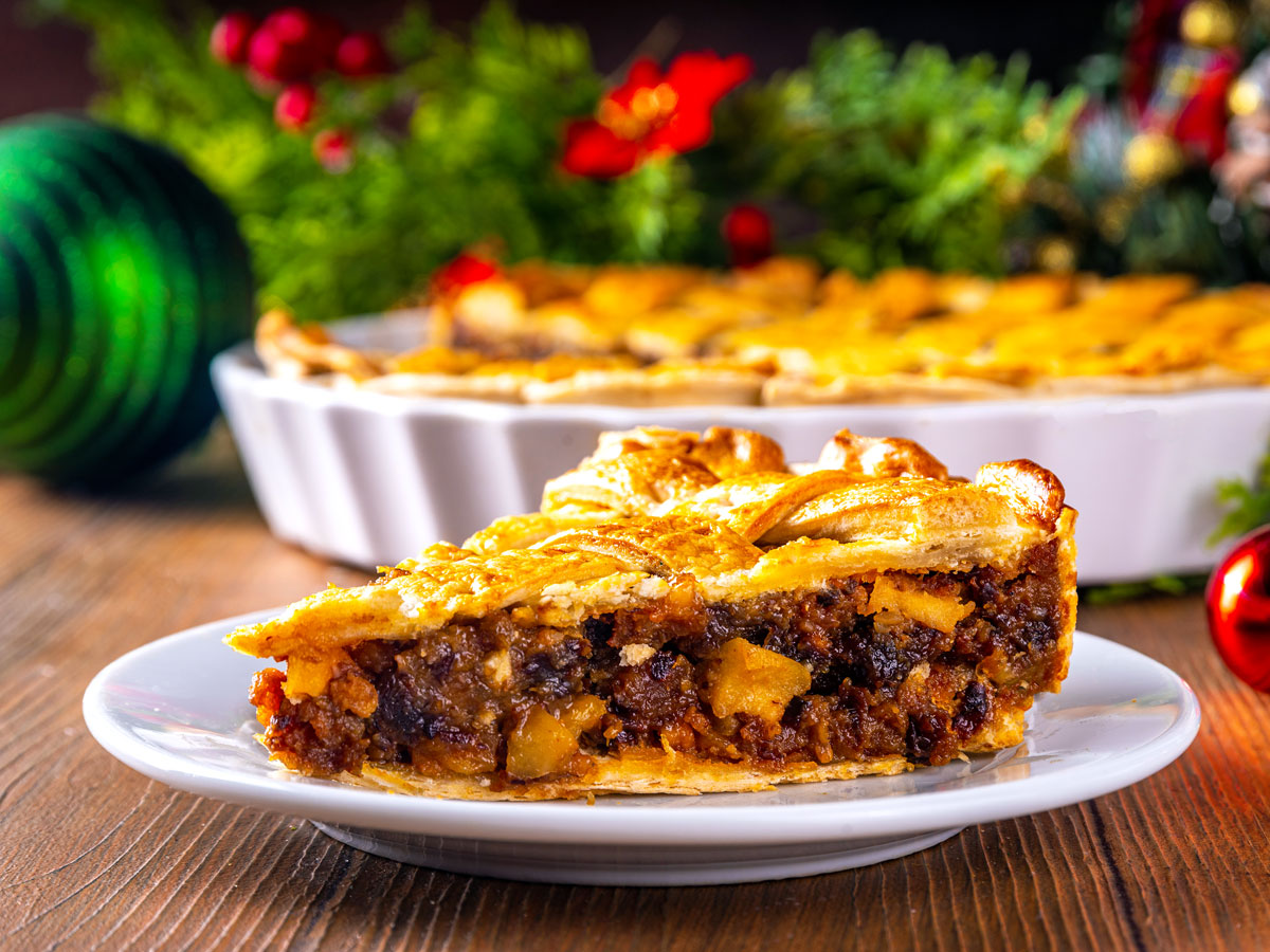 Slice of tourtière on plate with full pie and Christmas decorations on table