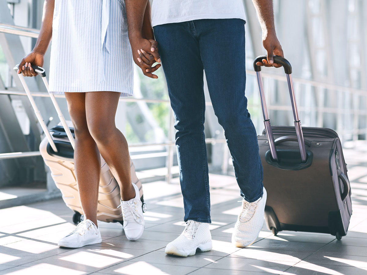 Couple holding hands and rolling luggage through airport terminal