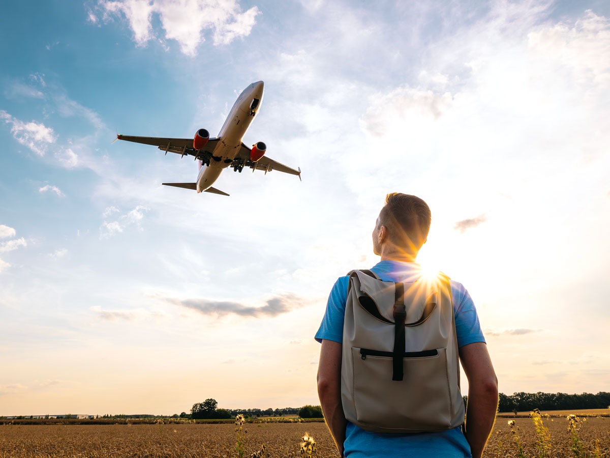 Person wearing backpack watching airplane take off overhead
