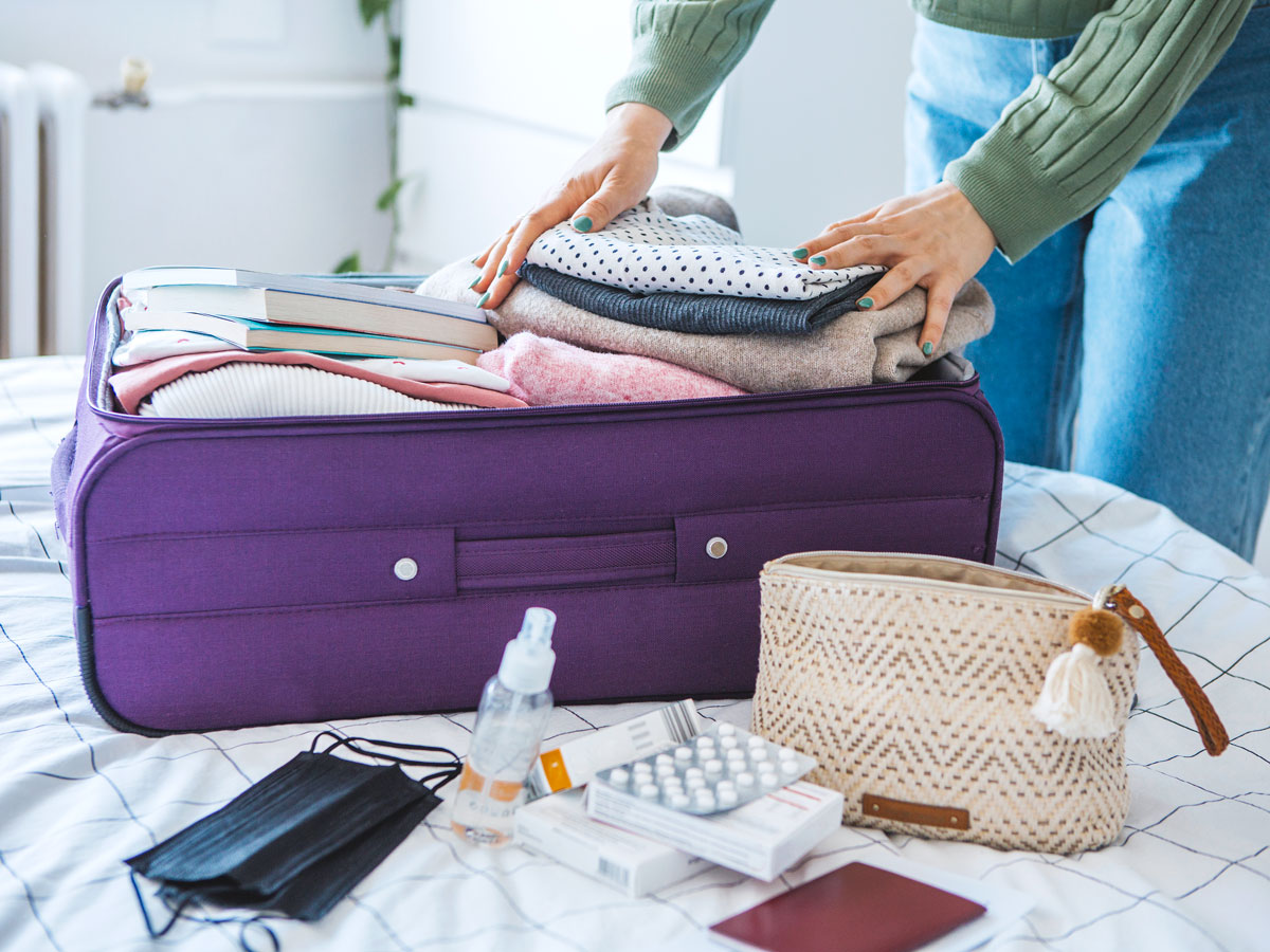 Person packing items in suitcase on bed