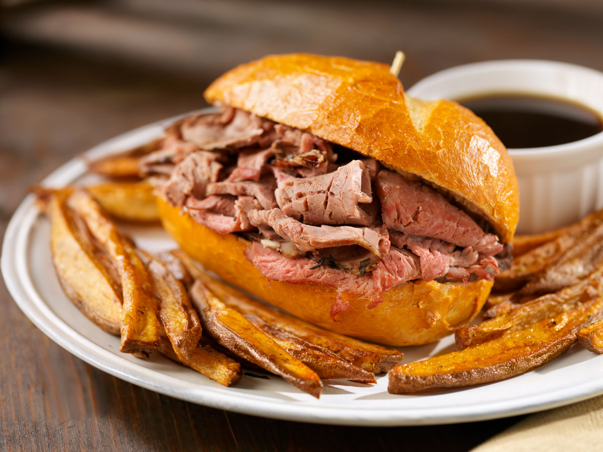 A French dip sandwich with fries and side of jus on a plate