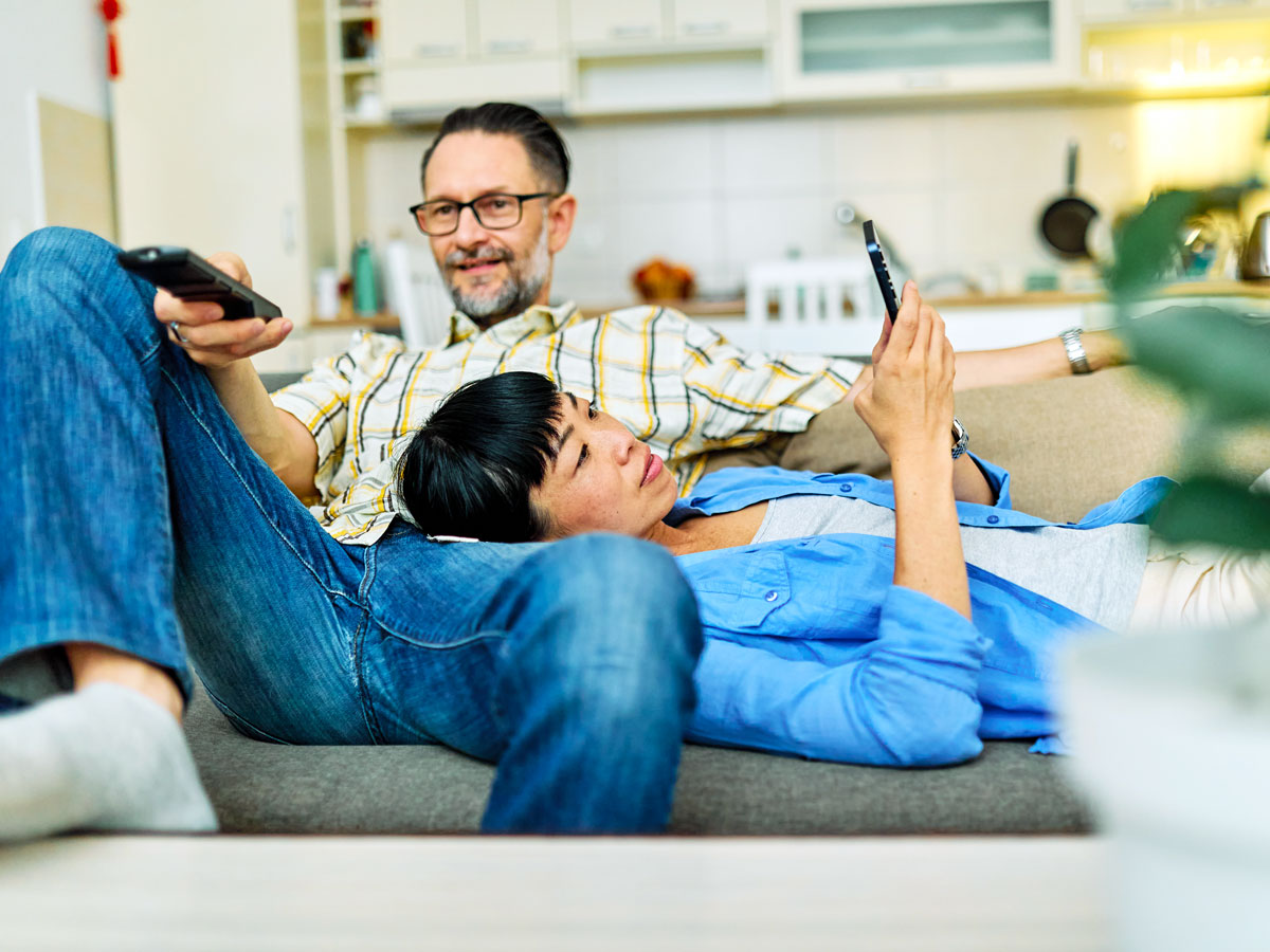 Woman reading book as man uses TV remote
